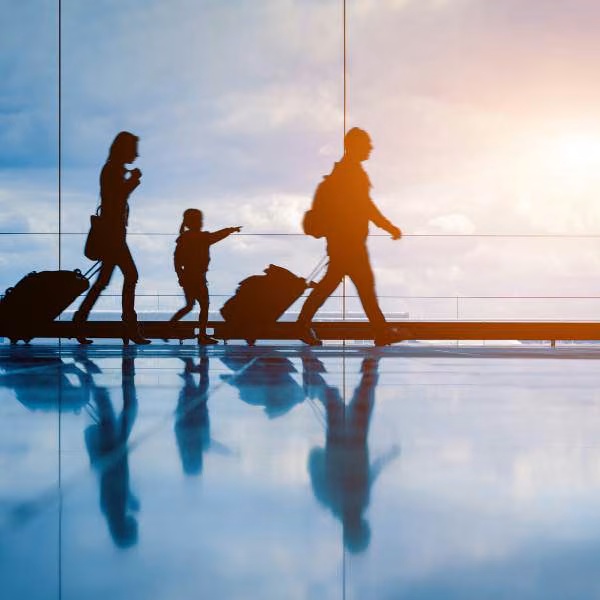Silhouettes of two adults and a child walking through an airport with luggage